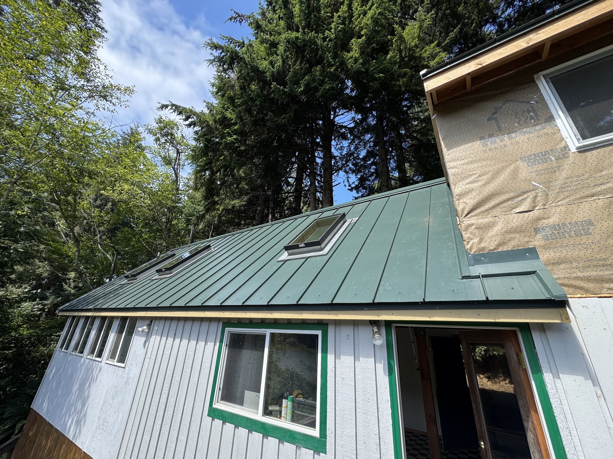 Green standing-seam metal roof panels installed with house wrap protected during construction