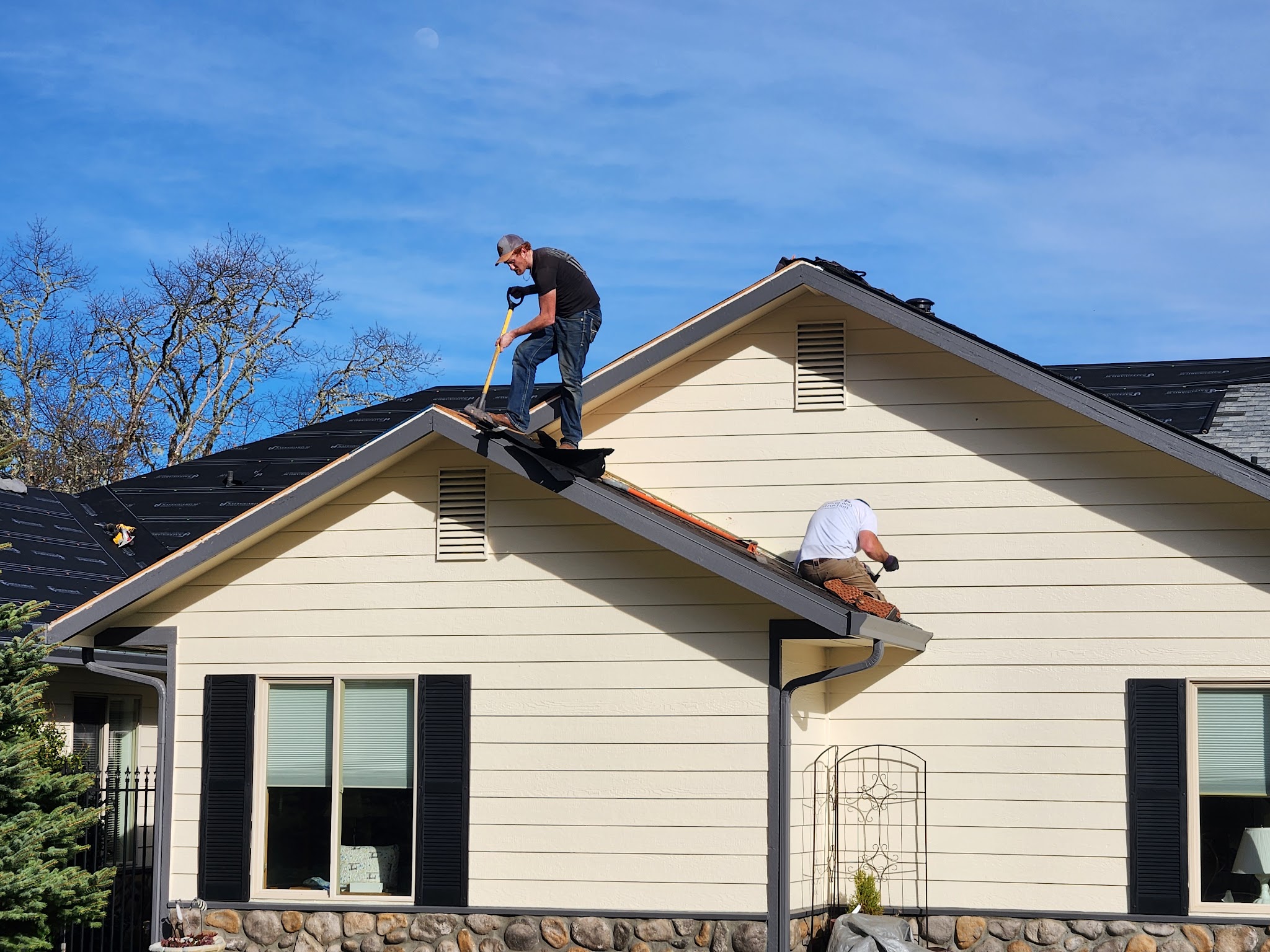 Two roofers tearing off and installing new shingles on a roof gable